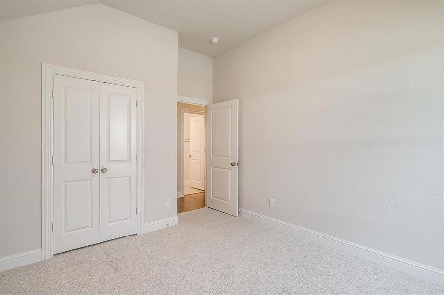 Unfurnished bedroom with light carpet, vaulted ceiling, and a closet