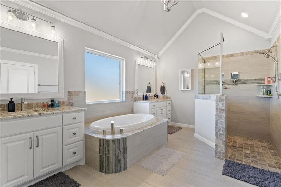 Bathroom with two vanities, ornamental molding, vaulted ceiling, a sink, and a bath