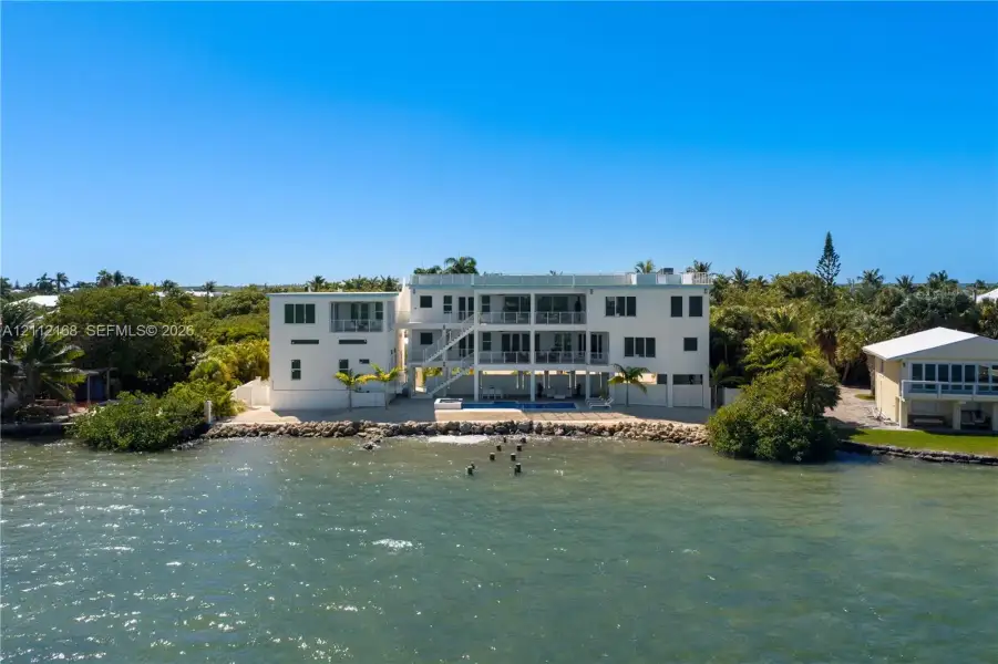Waterfront multi-story residence featuring tiered exterior balconies, a ground-level swimming pool, and stone-reinforced shoreline Waterfront multi-story residence featuring tiered exterior balconies, a ground-level swimming pool, and stone-reinforced shoreline