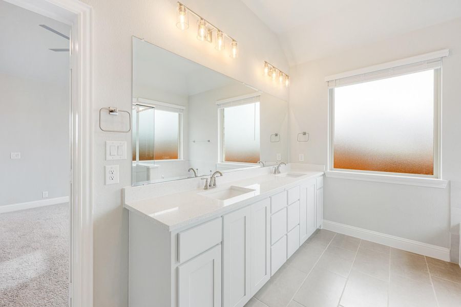 Bathroom with double sink vanity, white cabinets, large mirror, and frosted windows
