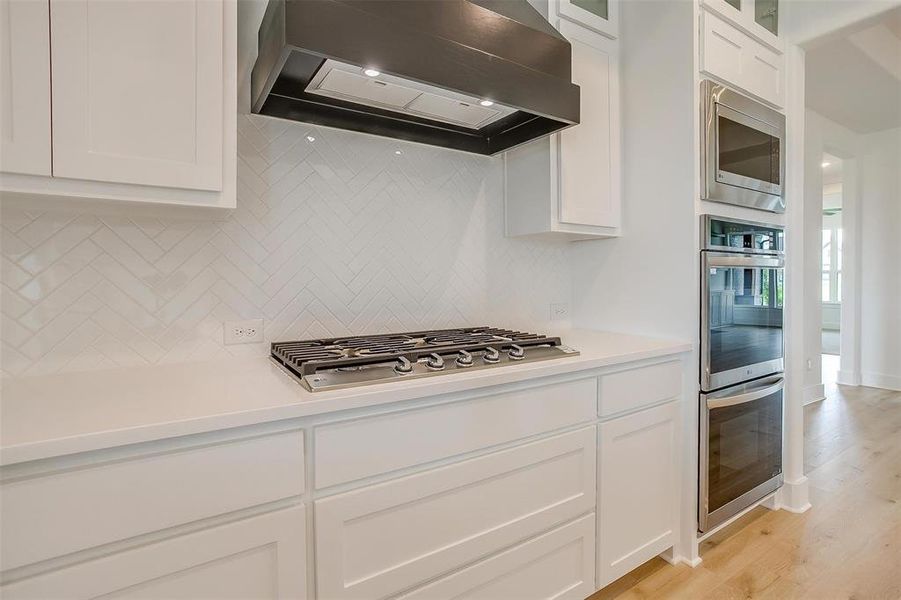 Kitchen featuring white cabinets, appliances with stainless steel finishes, light hardwood / wood-style floors, premium range hood, and tasteful backsplash