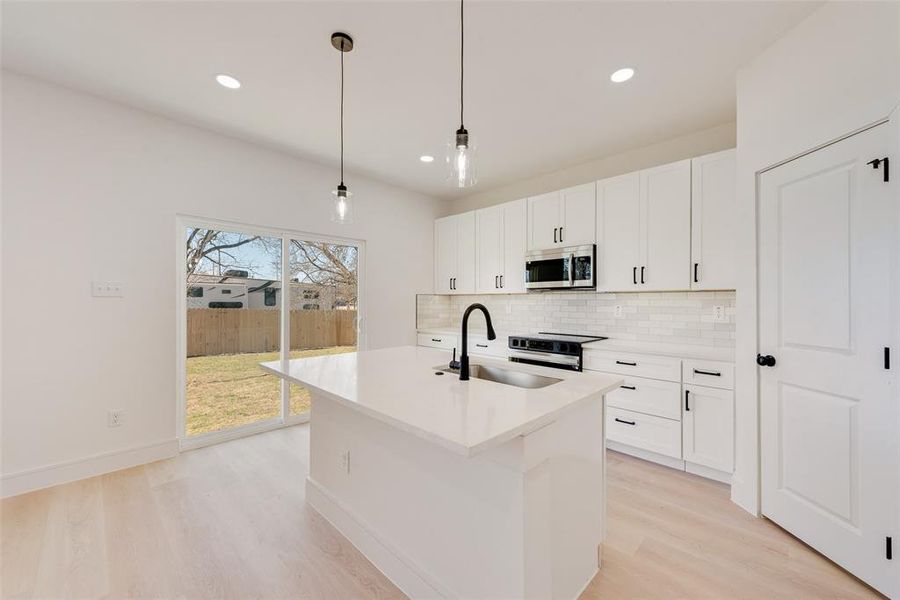 Kitchen with sink, light hardwood / wood-style floors, hanging light fixtures, and a kitchen island with sink