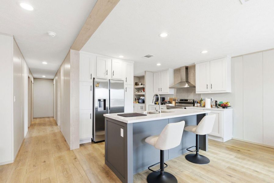 Kitchen featuring stainless steel appliances, white cabinets, light wood-style flooring, a kitchen bar, and recessed lighting