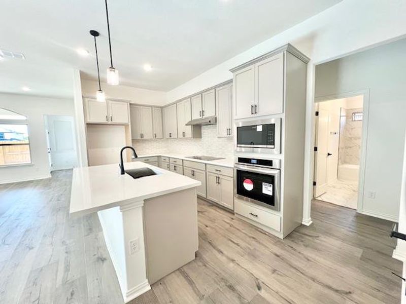 Kitchen featuring decorative backsplash, visible vents, appliances with stainless steel finishes, a sink, and light wood finished floors Kitchen featuring decorative backsplash, visible vents, appliances with stainless steel finishes, a sink, and light wood finished floors