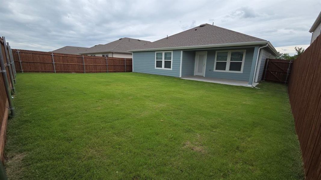 Spacious backyard featuring a large grass lawn, privacy fencing, and a concrete patio