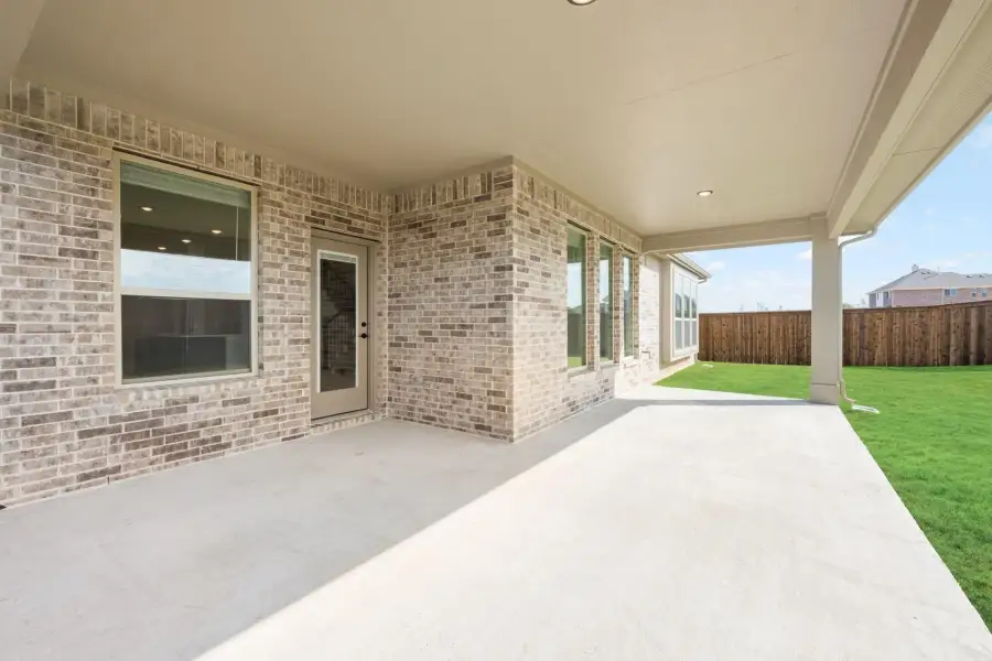 Covered back patio with concrete floor, brick exterior, and fenced backyard with green lawn