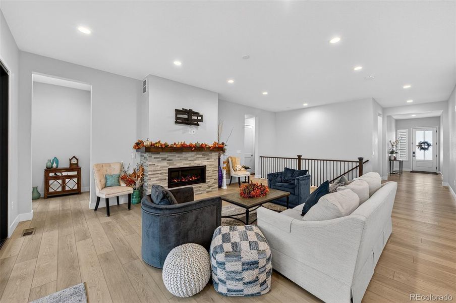 Living Room (Angle 1) – Open-concept living area centered around a sleek stone-surround fireplace and accented with recessed lighting and rich hardwood floors, perfect for relaxing or entertaining.