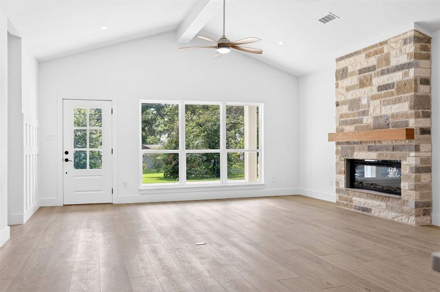 Spacious living area featuring a vaulted ceiling with exposed beam, wood-finish flooring, and a stone-clad fireplace with a natural wood mantel