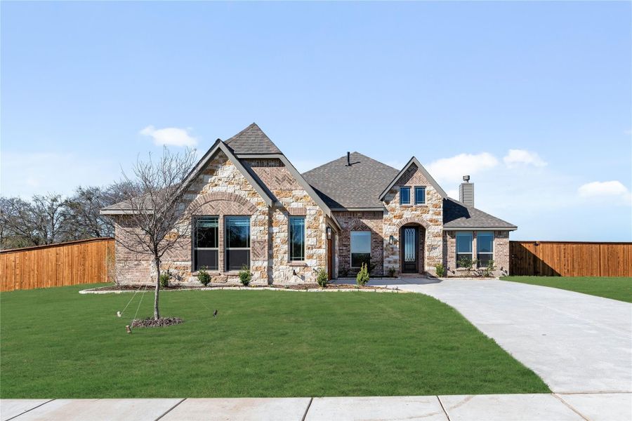 Single-story home with stone and brick exterior, arched entry, wide driveway, and fenced green lawn Single-story home with stone and brick exterior, arched entry, wide driveway, and fenced green lawn