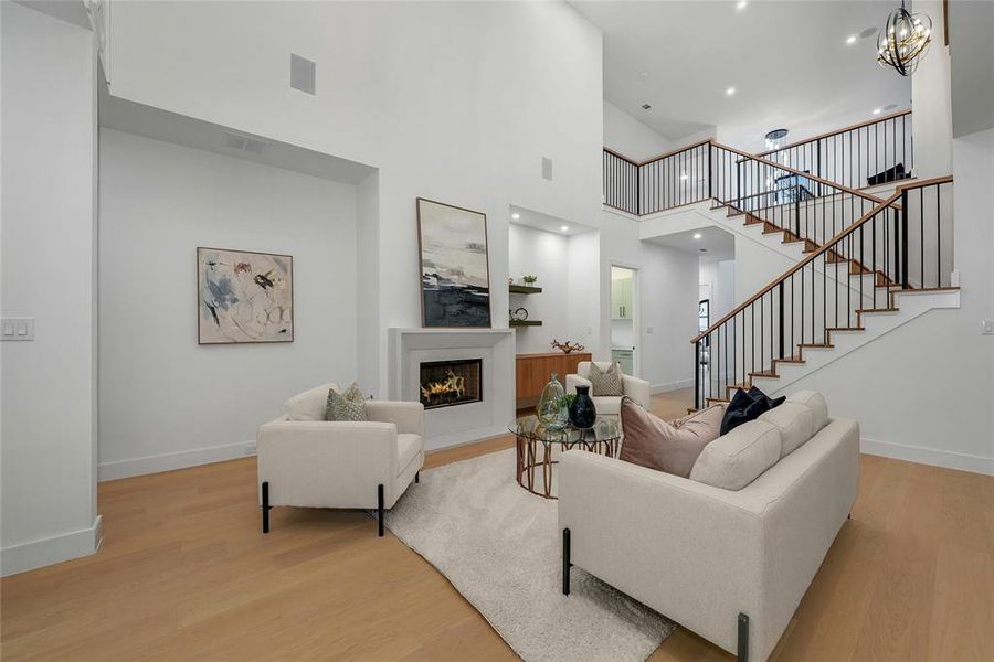 Living area featuring a warm lit fireplace, light wood finished floors, a high ceiling, and suspended lighting Living area featuring a warm lit fireplace, light wood finished floors, a high ceiling, and suspended lighting