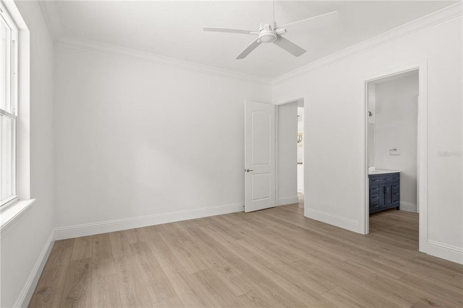 Downstairs primary bedroom featuring a neutral color palette, a ceiling fan, and an ensuite bathroom, offering a private and comfortable retreat.