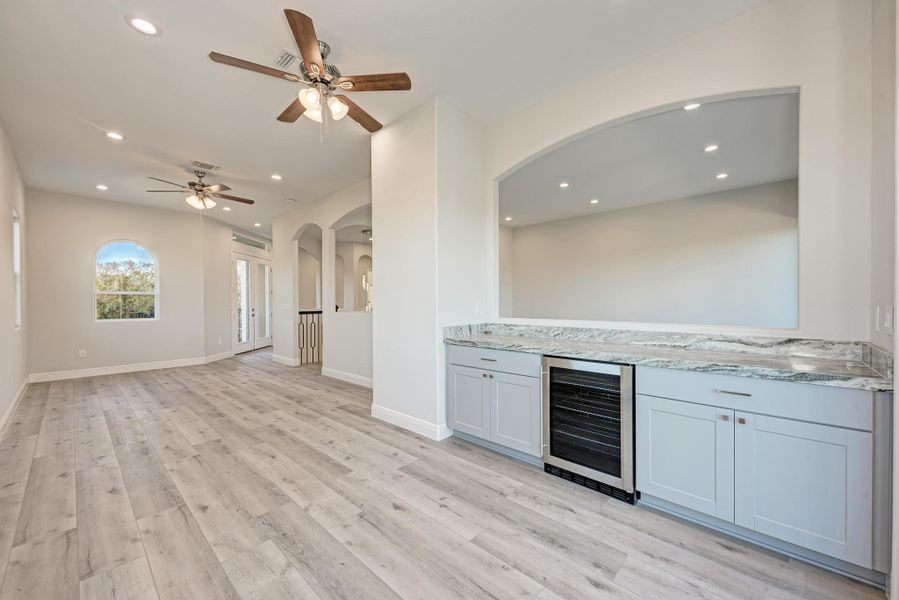 Bar with wine cooler, light stone counters, recessed lighting, arched walkways, and light wood-style flooring