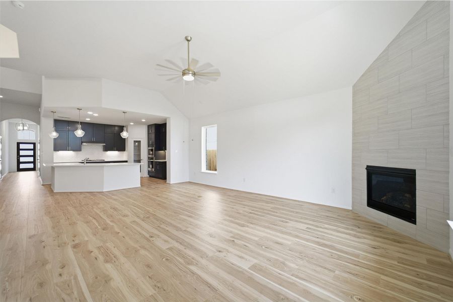 Unfurnished living room featuring ceiling fan, a tile fireplace, vaulted ceiling, arched walkways, and light wood-style floors
