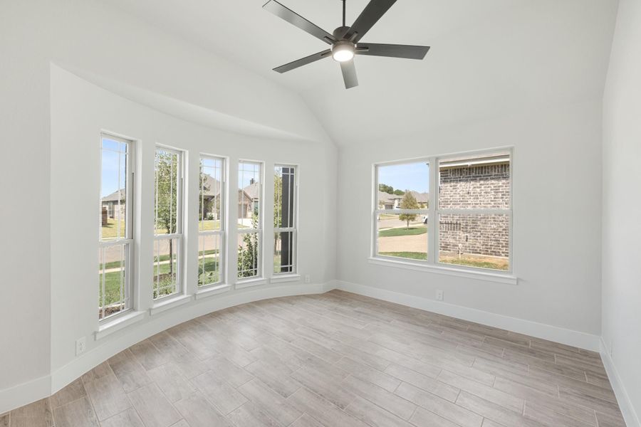 Empty room with vaulted ceiling, ceiling fan, multiple windows, and wood-look tile floors