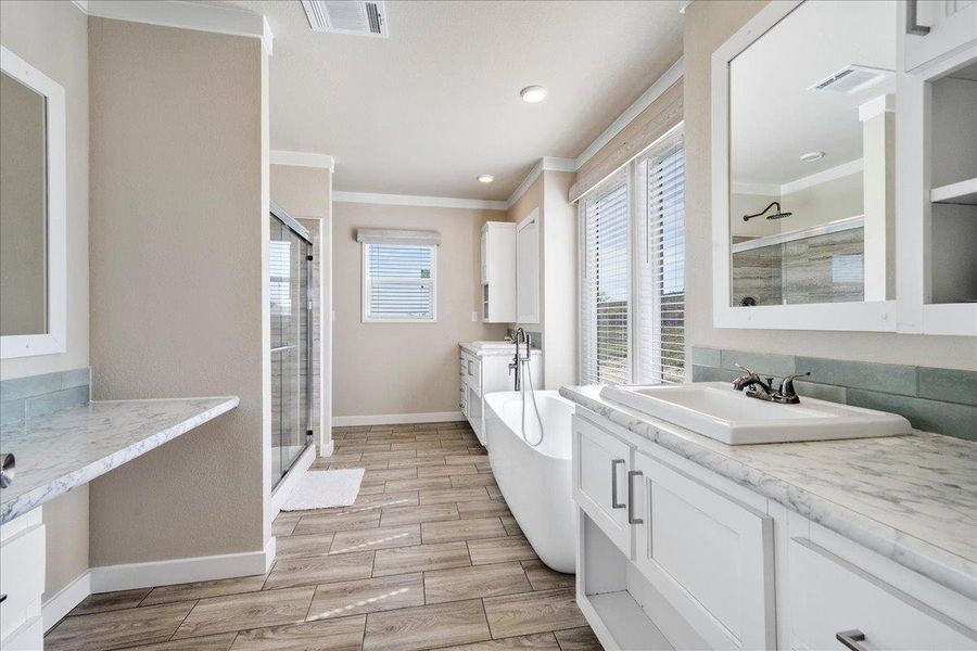 Bathroom with two vanities, wood finish floors, crown molding, a stall shower, and a freestanding bath Bathroom with two vanities, wood finish floors, crown molding, a stall shower, and a freestanding bath