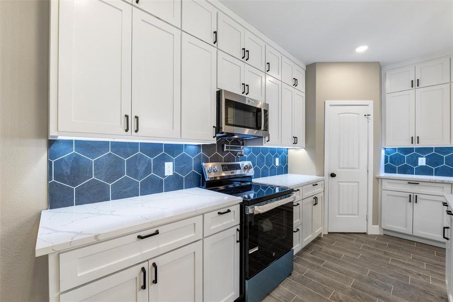 Kitchen with white cabinetry, light stone counters, and stainless steel appliances