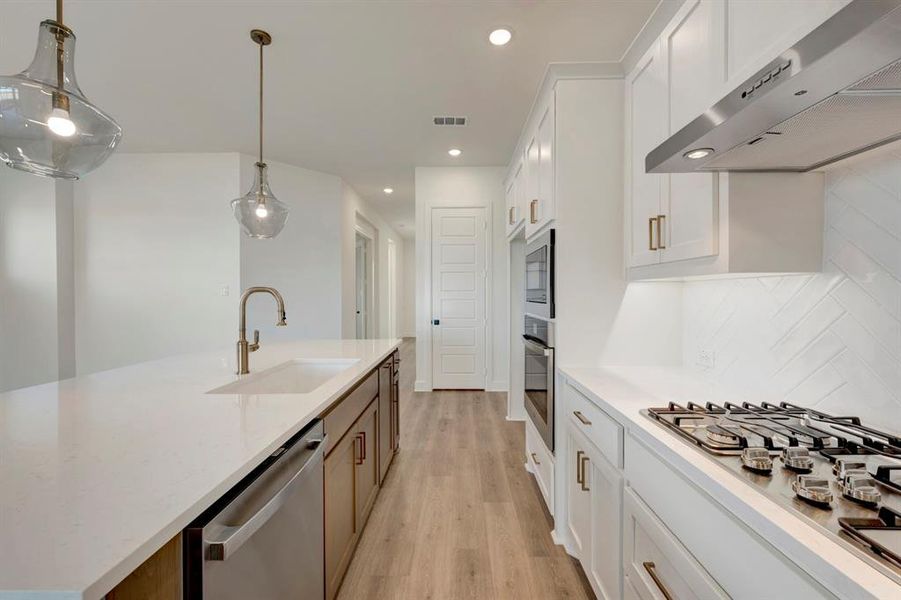 Kitchen featuring dual tone cabinets, stainless steel appliances, light wood finished floors, decorative light fixtures, and light stone countertops Kitchen featuring dual tone cabinets, stainless steel appliances, light wood finished floors, decorative light fixtures, and light stone countertops