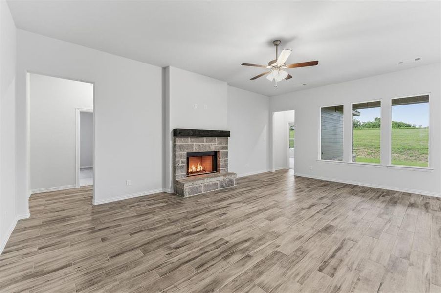 Living room featuring a stone-clad fireplace with a dark mantel, wood-finish flooring, and multiple windows