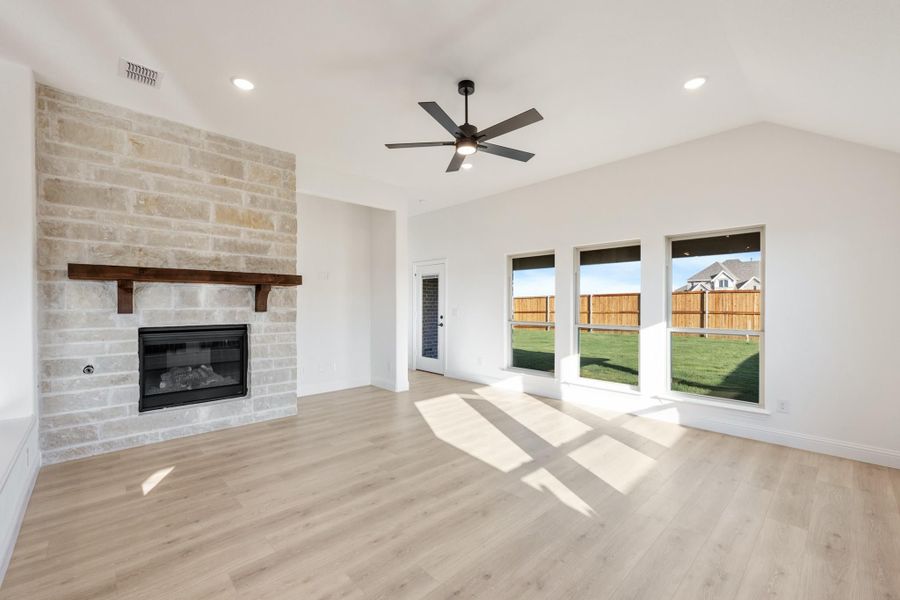 Open living room with floor-to-ceiling stone fireplace, wood mantel, ceiling fan, and light hardwood floors Open living room with floor-to-ceiling stone fireplace, wood mantel, ceiling fan, and light hardwood floors