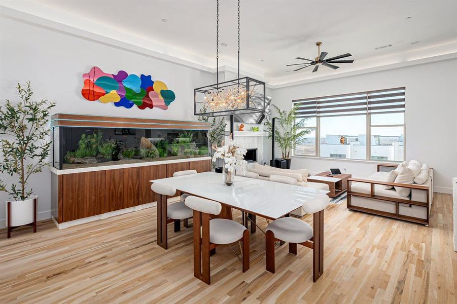 Dining room with a fireplace, ceiling fan with notable chandelier, light hardwood / wood-style floors, and a raised ceiling