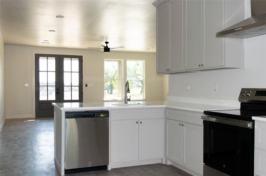 Kitchen with stainless steel appliances, wall chimney exhaust hood, a peninsula, french doors, and ceiling fan Kitchen with stainless steel appliances, wall chimney exhaust hood, a peninsula, french doors, and ceiling fan