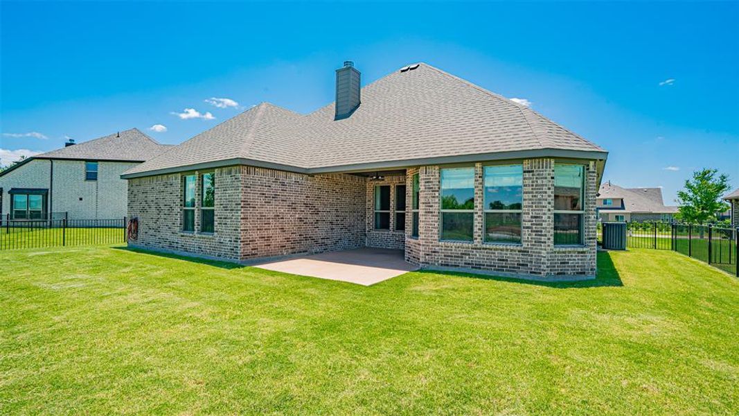 Expansive backyard featuring a manicured lawn, a covered concrete patio, multi-pane windows, and a brick exterior with a shingled roof