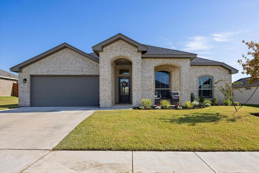 French country inspired facade featuring a front lawn, brick siding, concrete driveway, and an attached garage