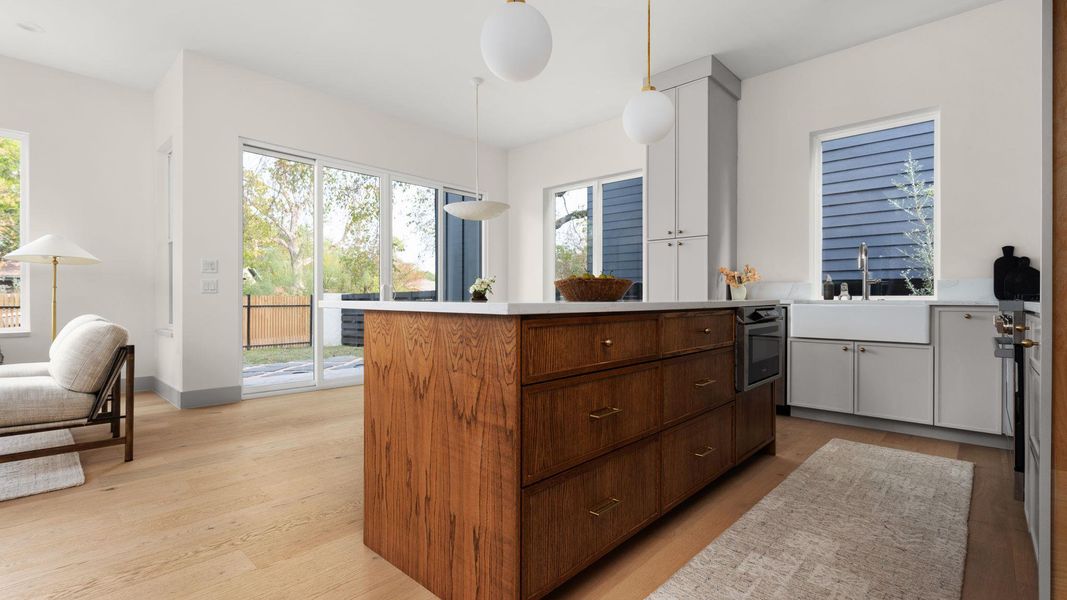 Kitchen with light countertops, a center island, light wood finished floors, decorative light fixtures, and white cabinets