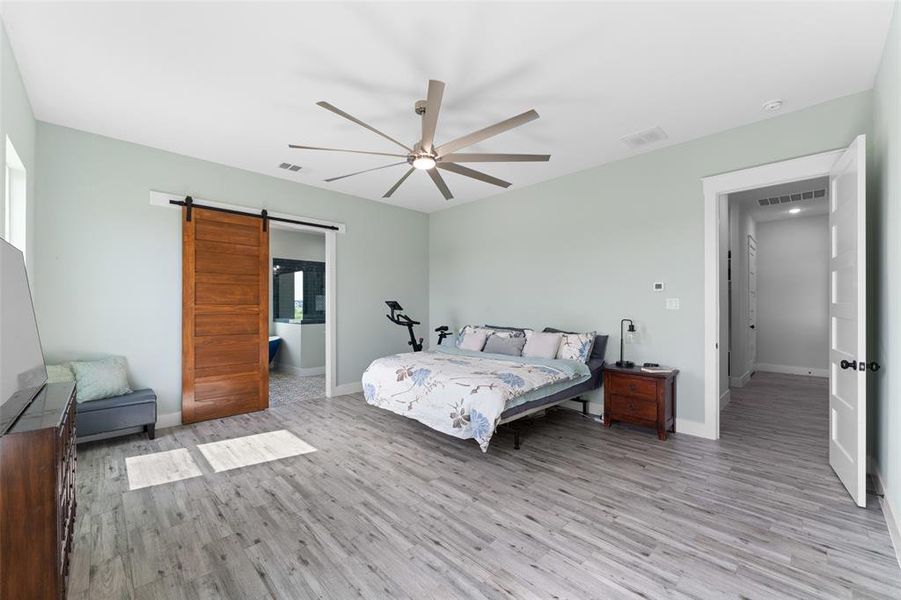 Spacious room featuring wood-finish flooring, a contemporary ceiling fan, and a barn door leading to an adjoining area