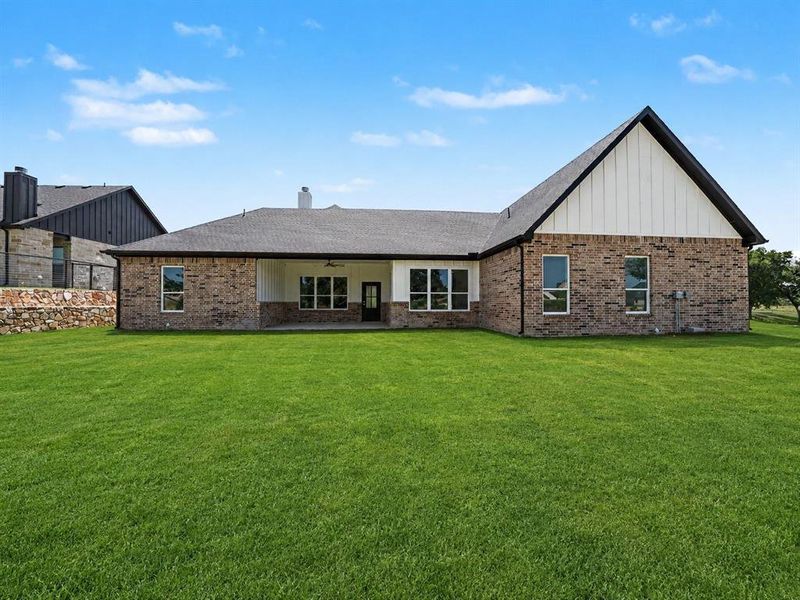 Expansive backyard featuring a manicured lawn, a covered patio with ceiling fan, and a brick exterior with white vertical siding accents