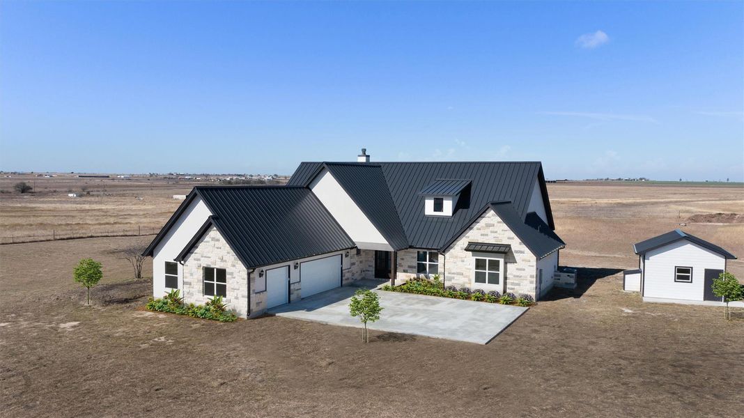 View of front facade featuring stone siding, an outdoor structure, concrete driveway, a metal roof, and a view of rural / pastoral area. Virtual staging used