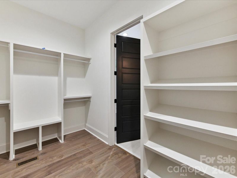 Spacious walk-in primary closet with custom built-in shelving and hanging space for organized storage.
