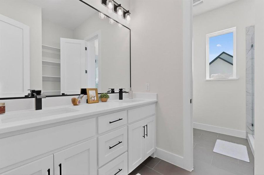 Full bath with double vanity, dark tile patterned flooring, and a marble finish shower