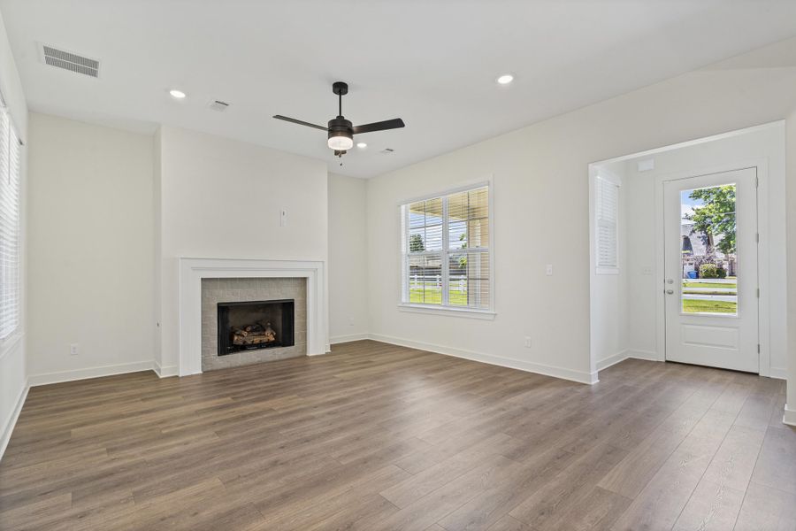 Spacious living area featuring wood-finish flooring, a fireplace with a tiled surround and white mantel, a ceiling fan with integrated lighting, recessed lighting, and a glass-paneled exterior door