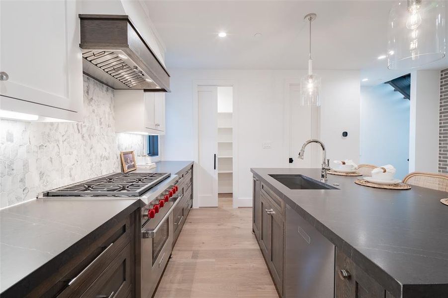 Kitchen with sink, hanging light fixtures, high end stainless steel range, light hardwood / wood-style floors, and custom range hood