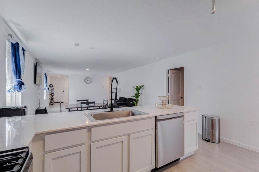 Spacious kitchen featuring a large island with breakfast bar seating, quartz countertops, stainless steel appliances, and an open view into the living and dining areas.