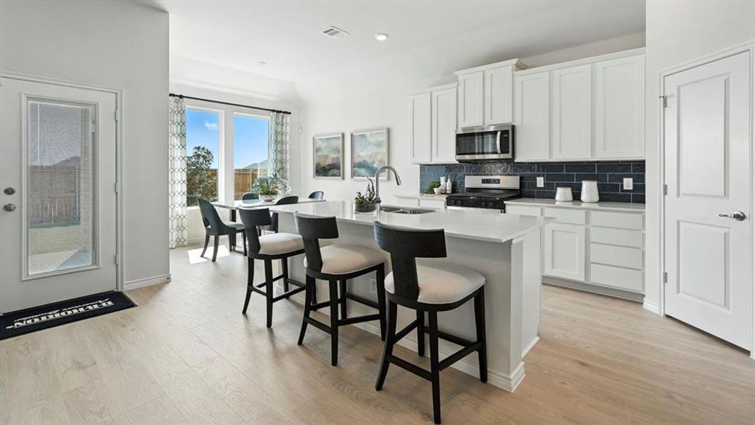 Open-concept kitchen and dining area featuring a central island, white cabinetry, stainless steel appliances, dark subway tile backsplash, and light wood-finish flooring