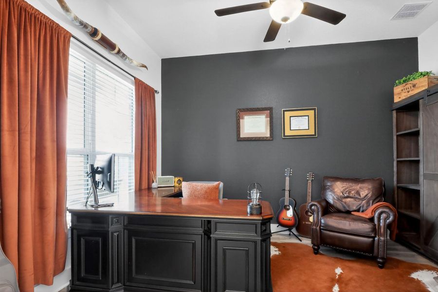 Dedicated room featuring a ceiling fan with integrated lighting, a large window with horizontal blinds, dark gray accent wall, and wood-finish flooring Dedicated room featuring a ceiling fan with integrated lighting, a large window with horizontal blinds, dark gray accent wall, and wood-finish flooring