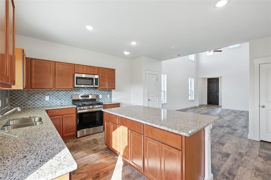 Kitchen with appliances with stainless steel finishes, brown cabinets, tasteful backsplash, a kitchen island, and light stone counters Kitchen with appliances with stainless steel finishes, brown cabinets, tasteful backsplash, a kitchen island, and light stone counters