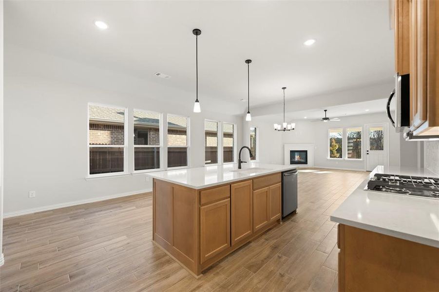 Kitchen with a glass covered fireplace, open floor plan, brown cabinetry, a center island with sink, and recessed lighting Kitchen with a glass covered fireplace, open floor plan, brown cabinetry, a center island with sink, and recessed lighting