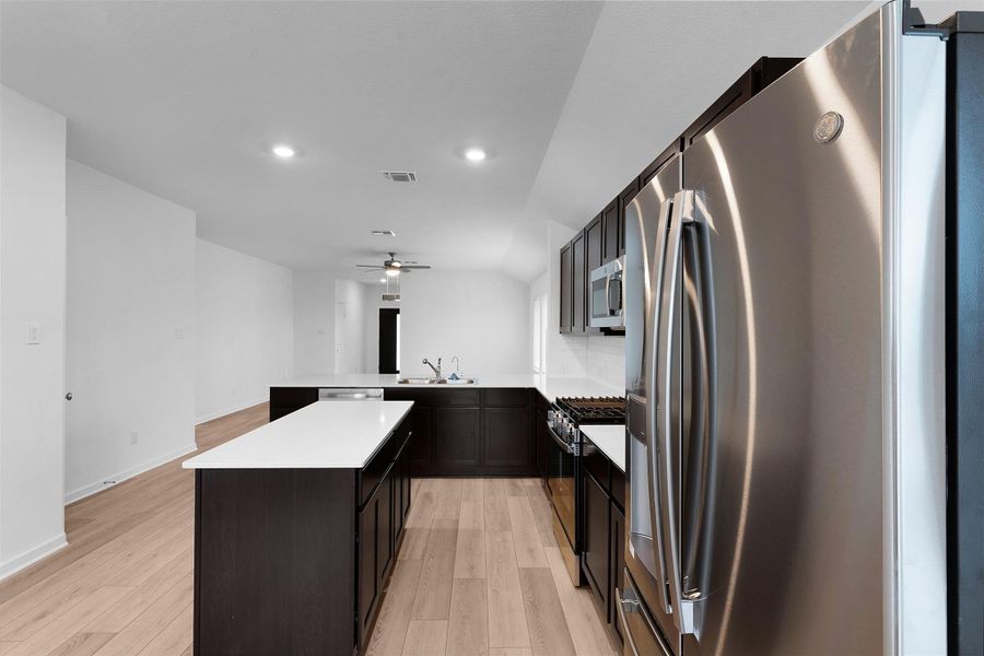 Kitchen featuring appliances with stainless steel finishes, light countertops, a peninsula, light wood-type flooring, and a center island