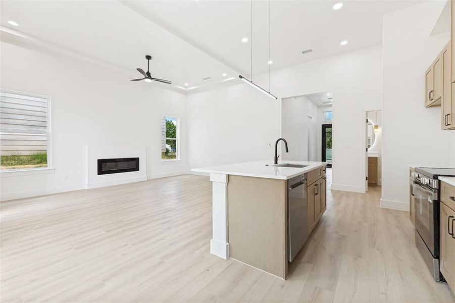 Open-concept living space featuring wood-finish flooring, a linear fireplace, and a recessed ceiling with a modern ceiling fan Open-concept living space featuring wood-finish flooring, a linear fireplace, and a recessed ceiling with a modern ceiling fan