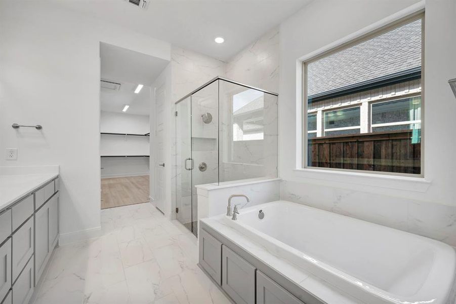 Bathroom featuring a spacious closet, a marble finish shower, light marble finish floors, vanity, and a bath Bathroom featuring a spacious closet, a marble finish shower, light marble finish floors, vanity, and a bath