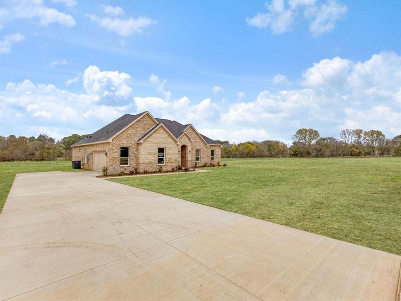 View of front of home with a front yard, stone siding, concrete driveway, brick siding, and a shingled roof View of front of home with a front yard, stone siding, concrete driveway, brick siding, and a shingled roof
