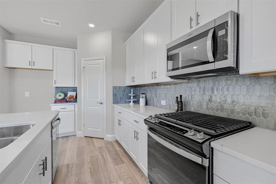 Kitchen featuring sink, tasteful backsplash, light hardwood / wood-style flooring, white cabinets, and appliances with stainless steel finishes