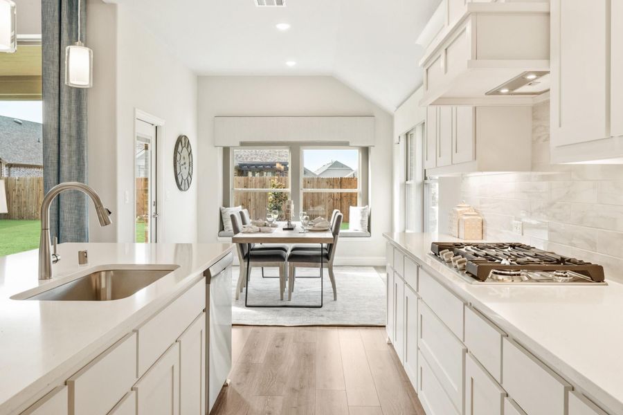 White kitchen with quartz countertops, gas cooktop, and open view to dining area with vaulted ceiling and hardwood floors. White kitchen with quartz countertops, gas cooktop, and open view to dining area with vaulted ceiling and hardwood floors.