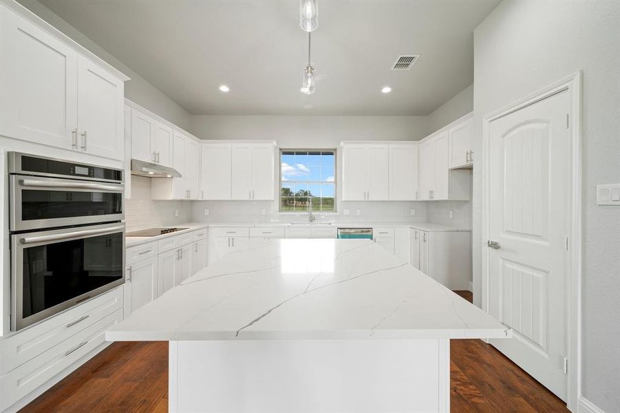 Kitchen with backsplash, light stone countertops, appliances with stainless steel finishes, and dark wood-type flooring