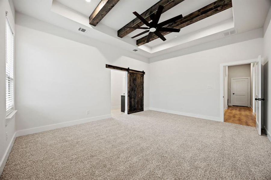 Unfurnished bedroom featuring light colored carpet, visible vents, beamed ceiling, and a barn door