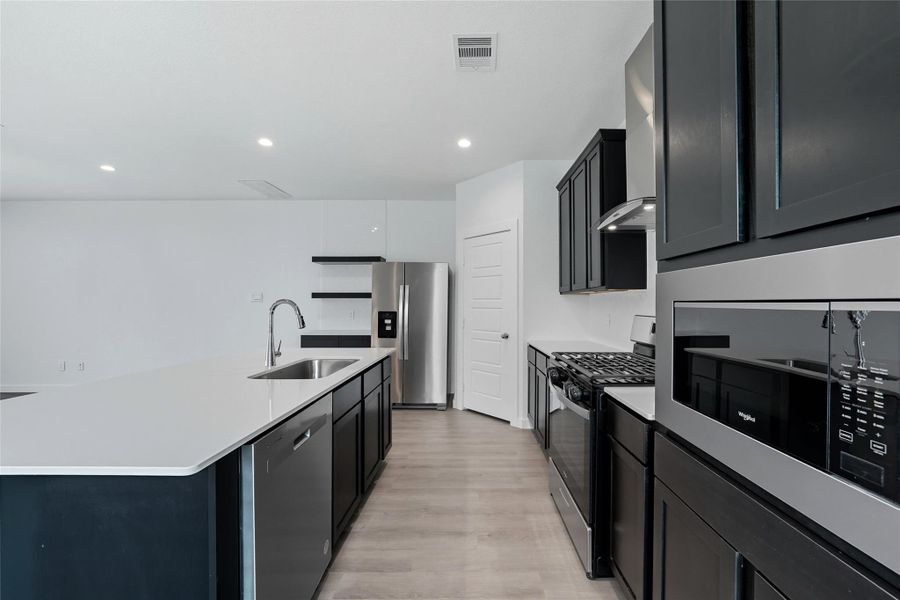 The sleek modern kitchen features quartz countertops, stainless steel appliances, gas range, built-in microwave, and dark cabinetry with ample storage. The large island offers room for bar seating, perfect for gatherings or meal time.