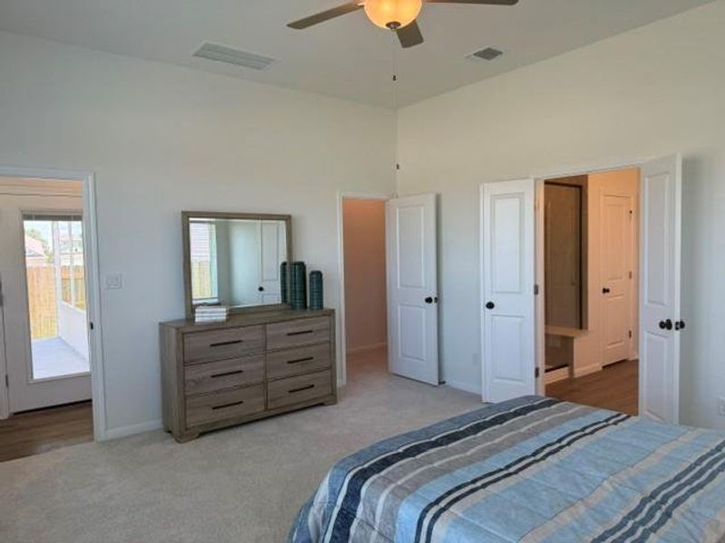 Spacious bedroom featuring vaulted ceilings, carpet flooring, a ceiling fan with integrated lighting, and multiple white paneled doors with black hardware